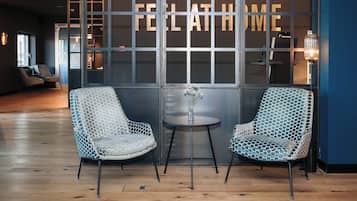 A modern interior with two patterned chairs, a small table with a vase, and a large window with the words 'FELLATHOME' visible.