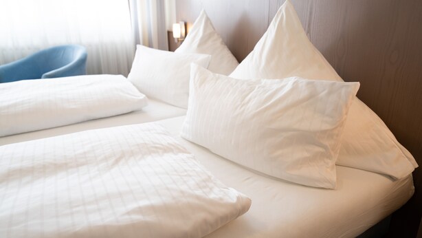A hotel room with a neatly made bed, a wooden headboard, and a blue chair. - ates Hotel Straßburg - Kehl (Kehl)