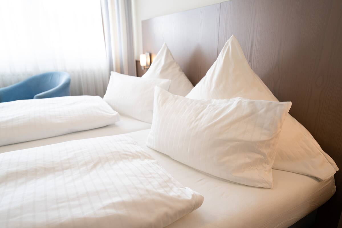 A hotel room with a neatly made bed, a wooden headboard, and a blue chair.