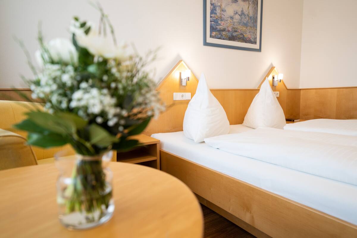 A neatly made bed with white pillows, a bedside table with a vase of flowers, and wall-mounted lights.