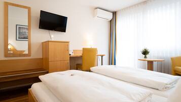A hotel room with two beds, a television, an air conditioning unit, a desk with a chair, and a small table with a plant.