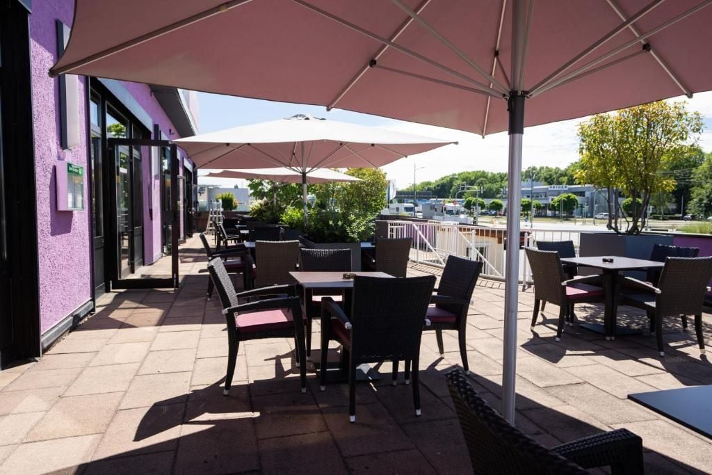 Een terras buiten met tafels en stoelen, parasols en een uitzicht op de stadslijn.