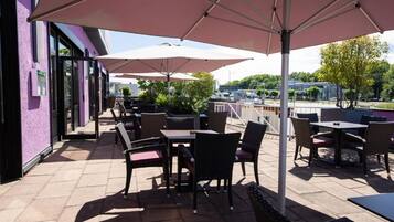 Een terras buiten met tafels en stoelen, parasols en een uitzicht op de stadslijn.