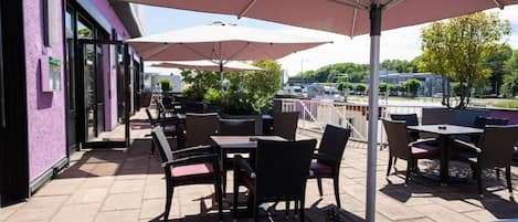An outdoor patio with tables and chairs, umbrellas, and a view of the cityscape.