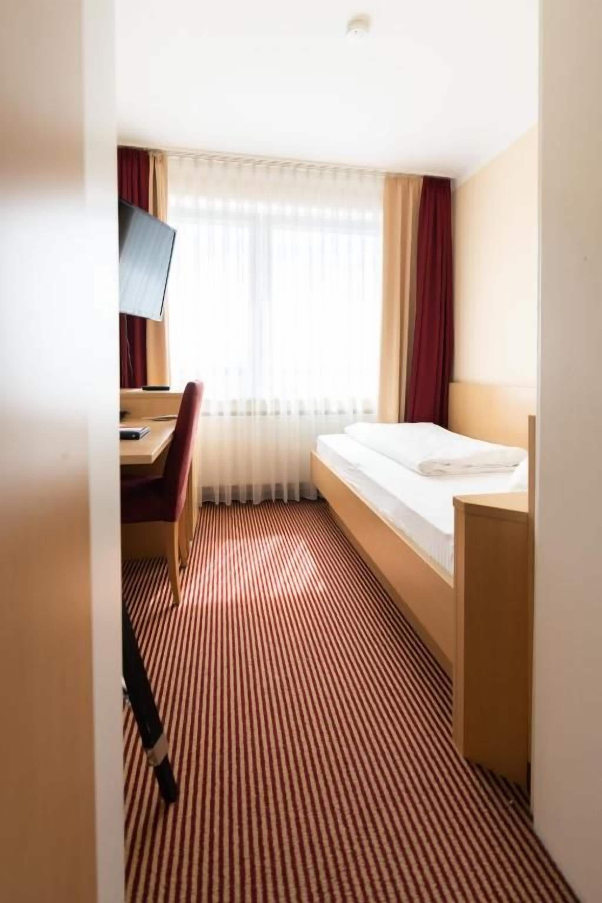 Una habitación de hotel con cama, escritorio con silla, televisor y ventana con cortinas.