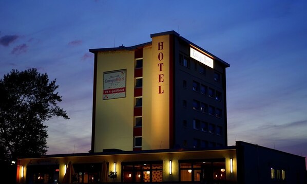 Ein Hotelgebäude mit einem gut sichtbaren 'HOTEL'-Schild an der Fassade, einem Schild mit der Aufschrift '24h geöffnet' und einem 'Europahotel'-Schild an der Seite.