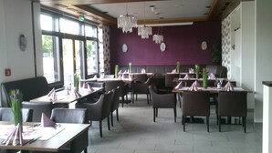 A restaurant with tables set for dining, purple walls, and hanging crystal chandeliers. - Europa Hotel (Kehl)