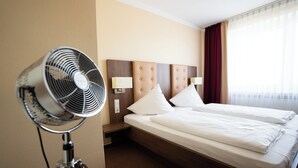 A hotel room with a bed, a standing fan, and a nightstand. - Europa Hotel (Kehl)