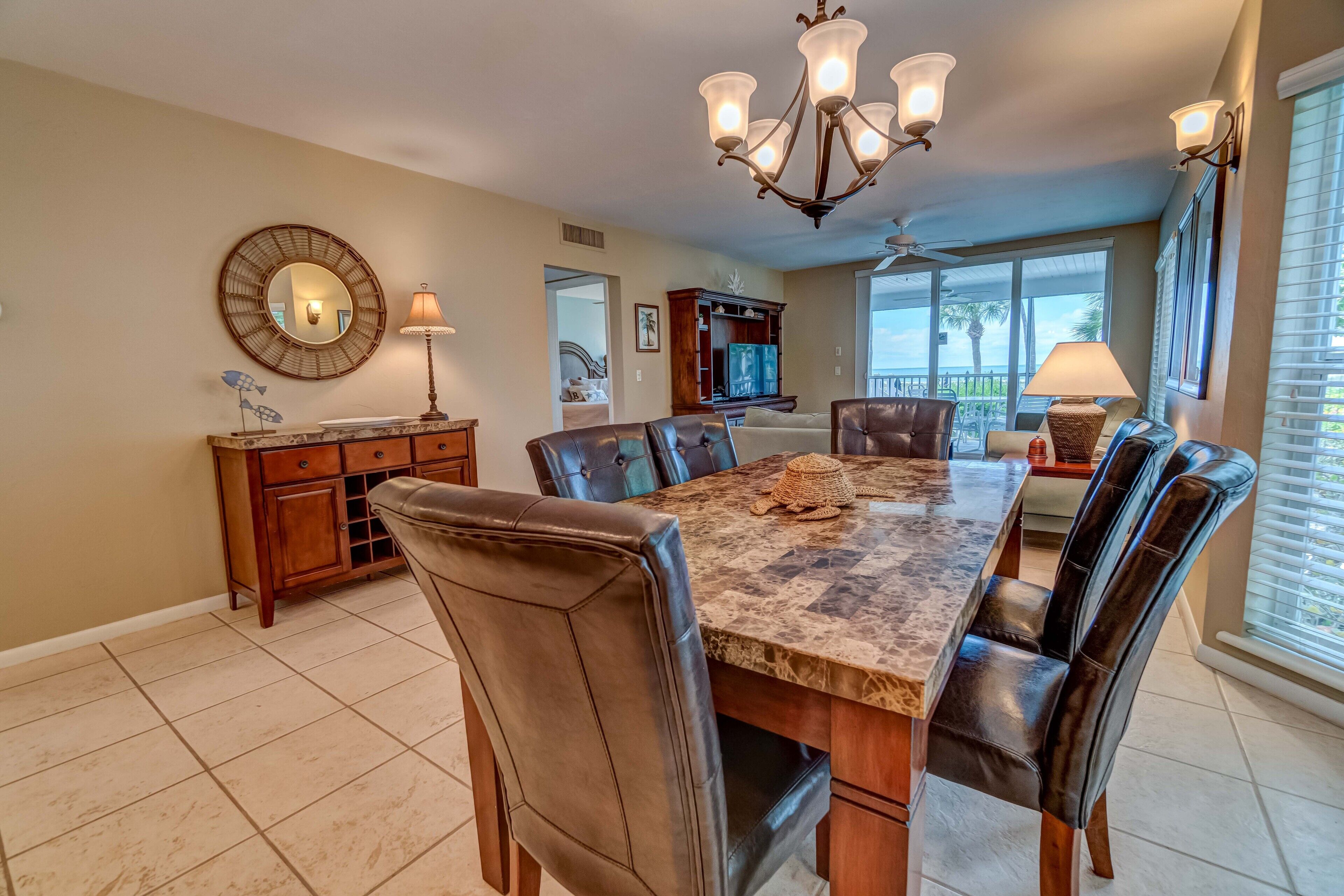 A dining room with a large marble table, leather chairs, a chandelier, and a view of the outdoors.