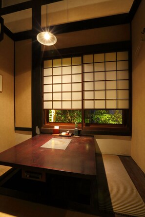 Une pièce de style japonais traditionnel, avec un sol recouvert de tatamis, une petite table en bois et une fenêtre à panneaux coulissants de type shoji.