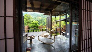 Een traditionele Japanse kamer met tatami vloeren, een houten plafond en een schuifdeur naar een balkon met uitzicht op een weelderig bos.