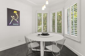 A modern dining area with a white round table, metal wire chairs, and a framed artwork on the wall.