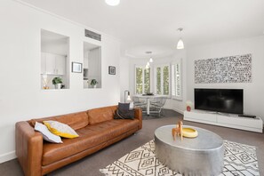 A modern living room with a brown leather sofa, a round coffee table, and a large flat-screen TV.