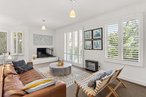 A modern living room with a leather sofa, a round coffee table, and a patterned rug. There is a fireplace, a television, and a set of framed pictures on the wall. - Wellington Mews Central East Melbourne Retreat (East Melbourne)