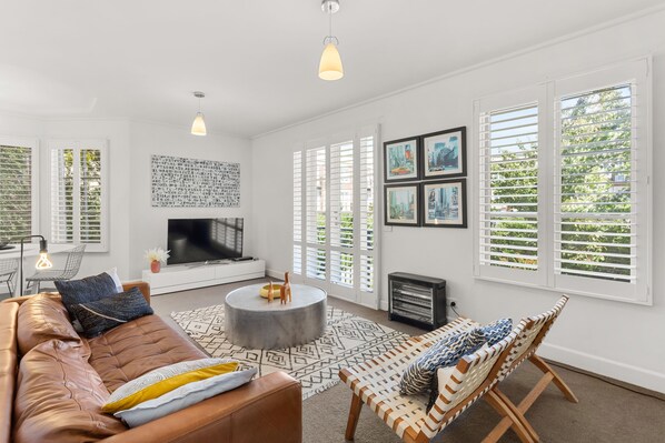 A modern living room with a leather sofa, a round coffee table, and a patterned rug. There is a fireplace, a television, and a set of framed pictures on the wall.