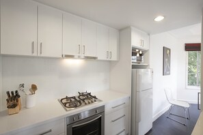 A modern kitchen with white cabinetry, a gas stove, a built-in oven, and a stainless steel refrigerator. - Wellington Mews Central East Melbourne Retreat (East Melbourne)