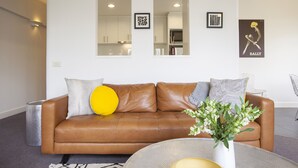 En moderne stue med en brun lædersofa, et rundt sofabord og en vase med blomster.