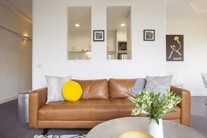 A modern living room with a brown leather sofa, a round coffee table, and a vase with flowers. - Wellington Mews Central East Melbourne Retreat (East Melbourne)