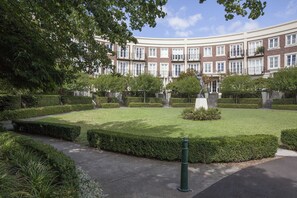 A well-maintained courtyard with neatly trimmed hedges, a statue, and a multi-story building with uniform windows in the background. - Wellington Mews Central East Melbourne Retreat (East Melbourne)