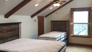 Quarto com uma cama grande, uma cama menor, janelas venezianas e um ventilador de teto.