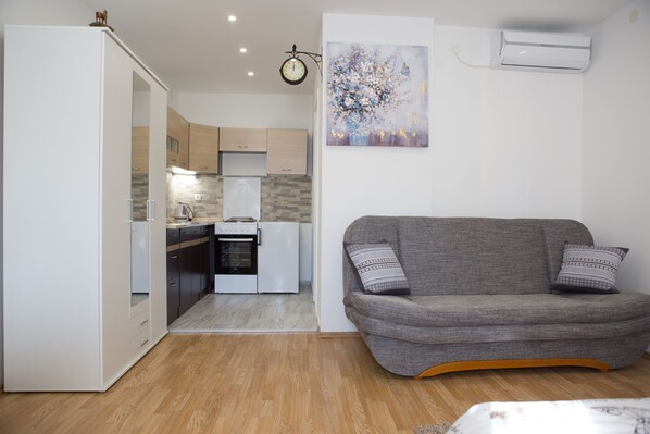A compact living space with a kitchenette, a grey sofa, and a painting on the wall.
