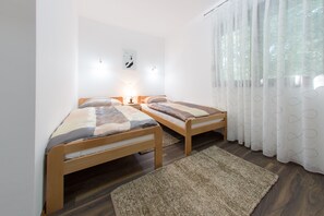 A bedroom with two wooden beds, a rug, a wall clock, and a window with sheer curtains.