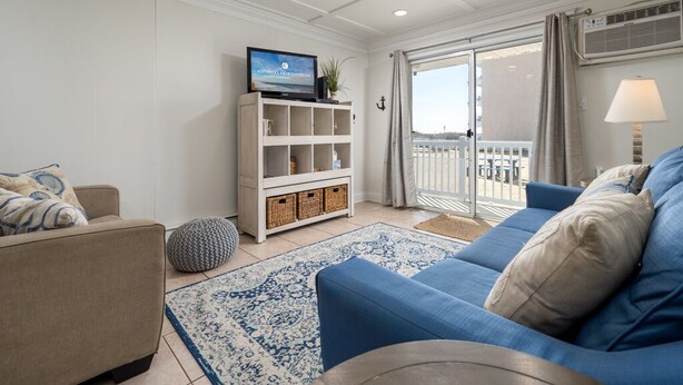 A living room with a blue sofa, beige armchair, white shelving unit, and a television. - Oceanfront condos with 3 night minimum rentals and linens included! (Ocean City)