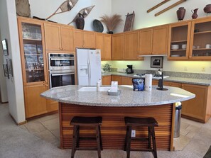 A kitchen with wooden cabinets, a central island with stools, a refrigerator, an oven, and a coffee maker. - Snowcreek Resort Vacation Rental 776 (Mammoth Lakes)