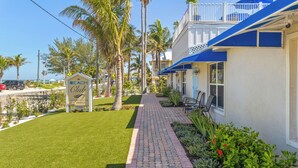 A beachfront hotel with a paved walkway, palm trees, and a sign indicating a vacancy. - Rooftop Sunsets 2 Bed Unit Beach Club AMI 4 by RVA (Bradenton Beach)