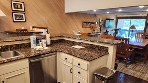 Een keuken met granieten aanrechtbladen, witte kasten, een roestvrijstalen vaatwasser en een vuilnisbak.