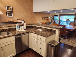 A kitchen with granite countertops, white cabinetry, a stainless steel dishwasher, and a trash can.