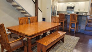 A dining area with a wooden table and chairs, a bench, a kitchen with white cabinets and appliances, and a staircase. - Snowcreek Resort Vacation Rental 92 (Mammoth Lakes)