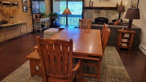 Une table à manger en bois avec des chaises, un canapé, une cheminée et une lampe.