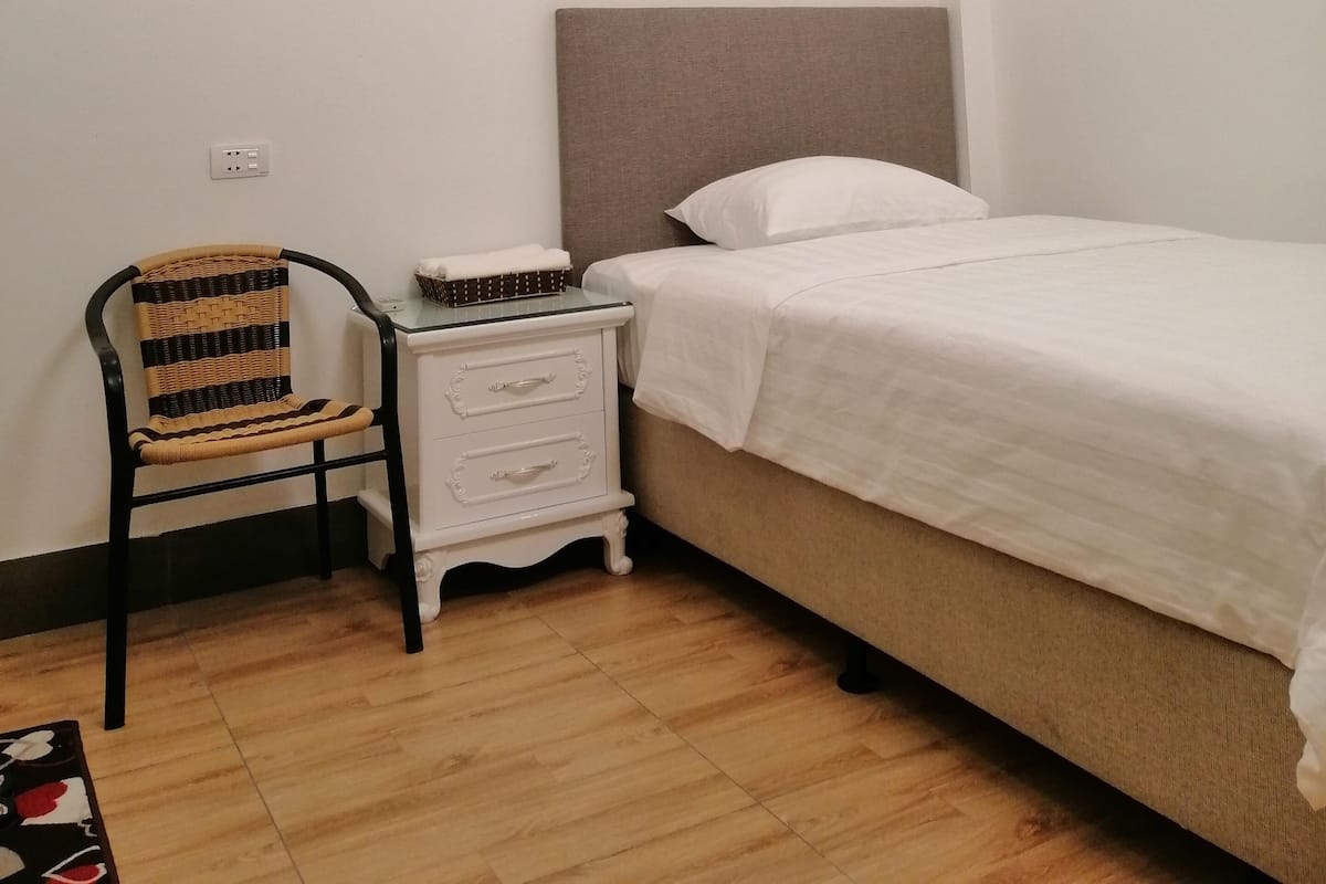 A bedroom with a single bed, a nightstand, a chair, and a small table.
