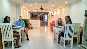 A dining area with four people seated at tables, a ceiling fan, and a staircase in the background. - Sao Mai Cosy Nest Noi Bai Airport (Hanoi)