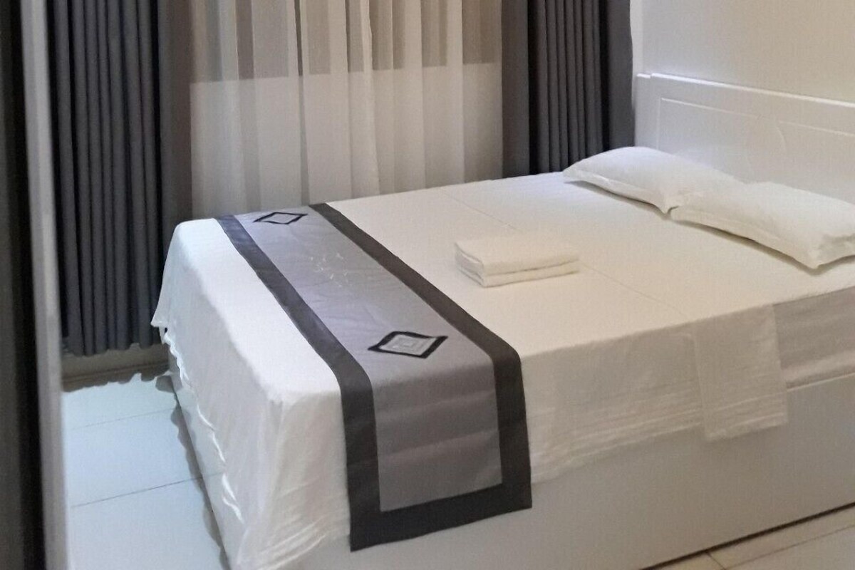Una habitación de hotel con cama, cortinas y una lámpara en el techo.