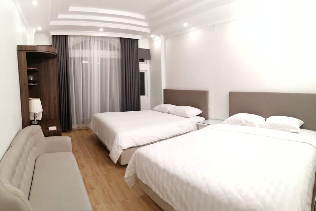 A hotel room with two beds, a sofa, a wooden wardrobe, and a large window with curtains.