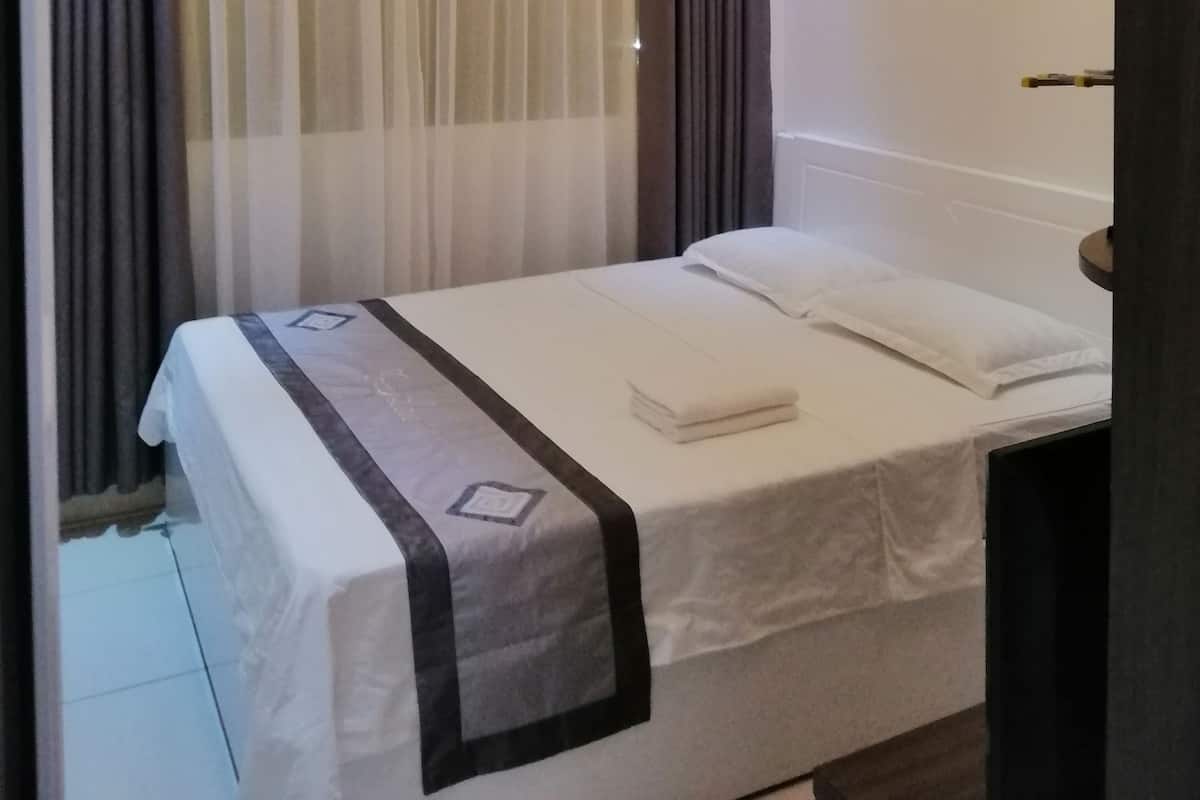 A hotel room with a neatly made bed, a bedside table, and a window with curtains.