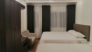 A modern hotel room with two beds, a wardrobe, a small seating area, and a large window with curtains. - Sao Mai Cosy Nest Noi Bai Airport (Hanoi)