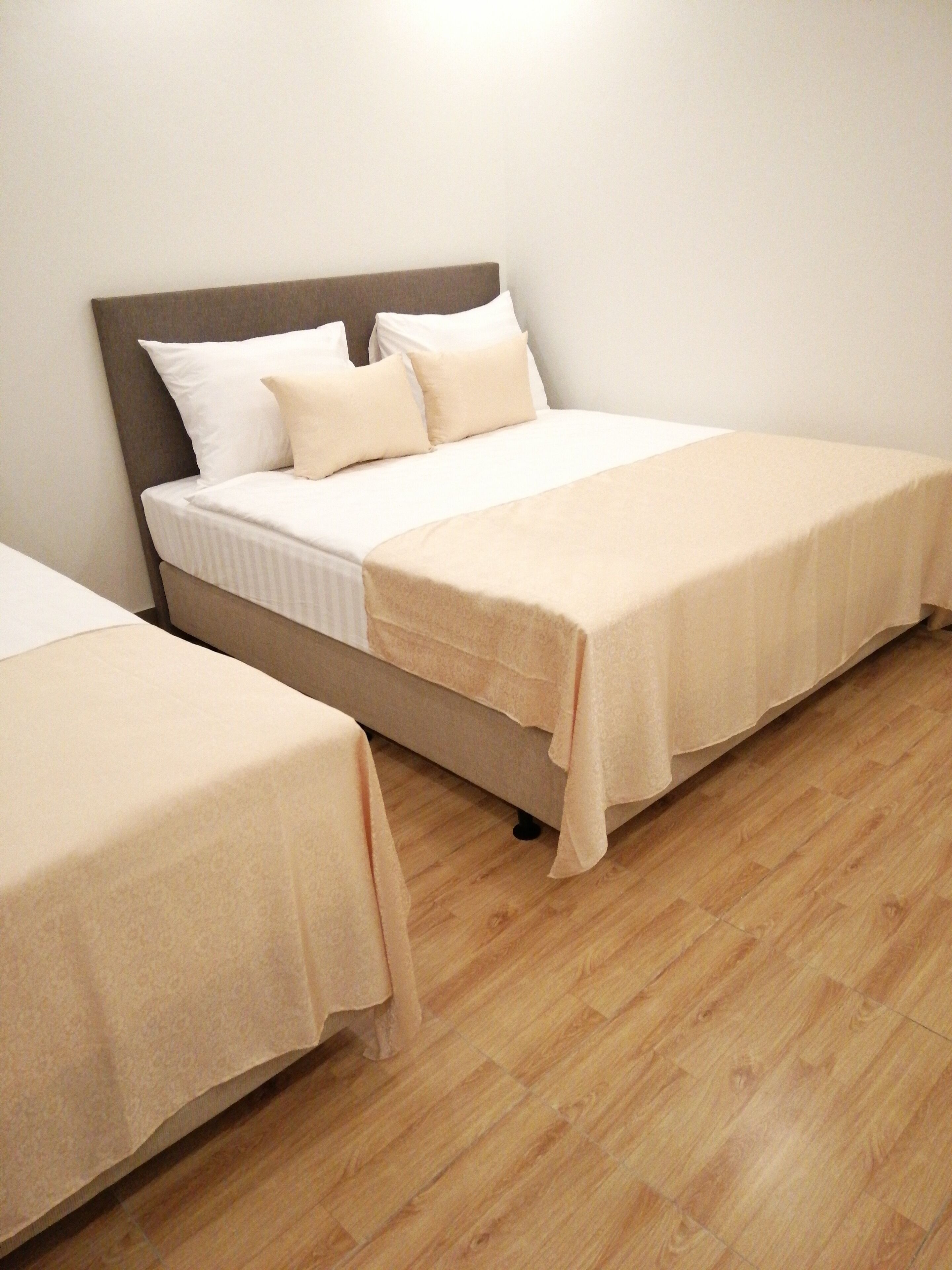 Ein Hotelzimmer mit zwei Einzelbetten, Holzboden und einer schlichten weißen Wand.