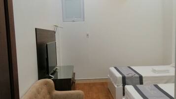 A room with a sofa, a TV, a ceiling fan, and two beds.