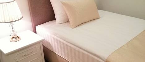 Una cama bien hecha con cabecera, mesita de noche con cajones y una lámpara.