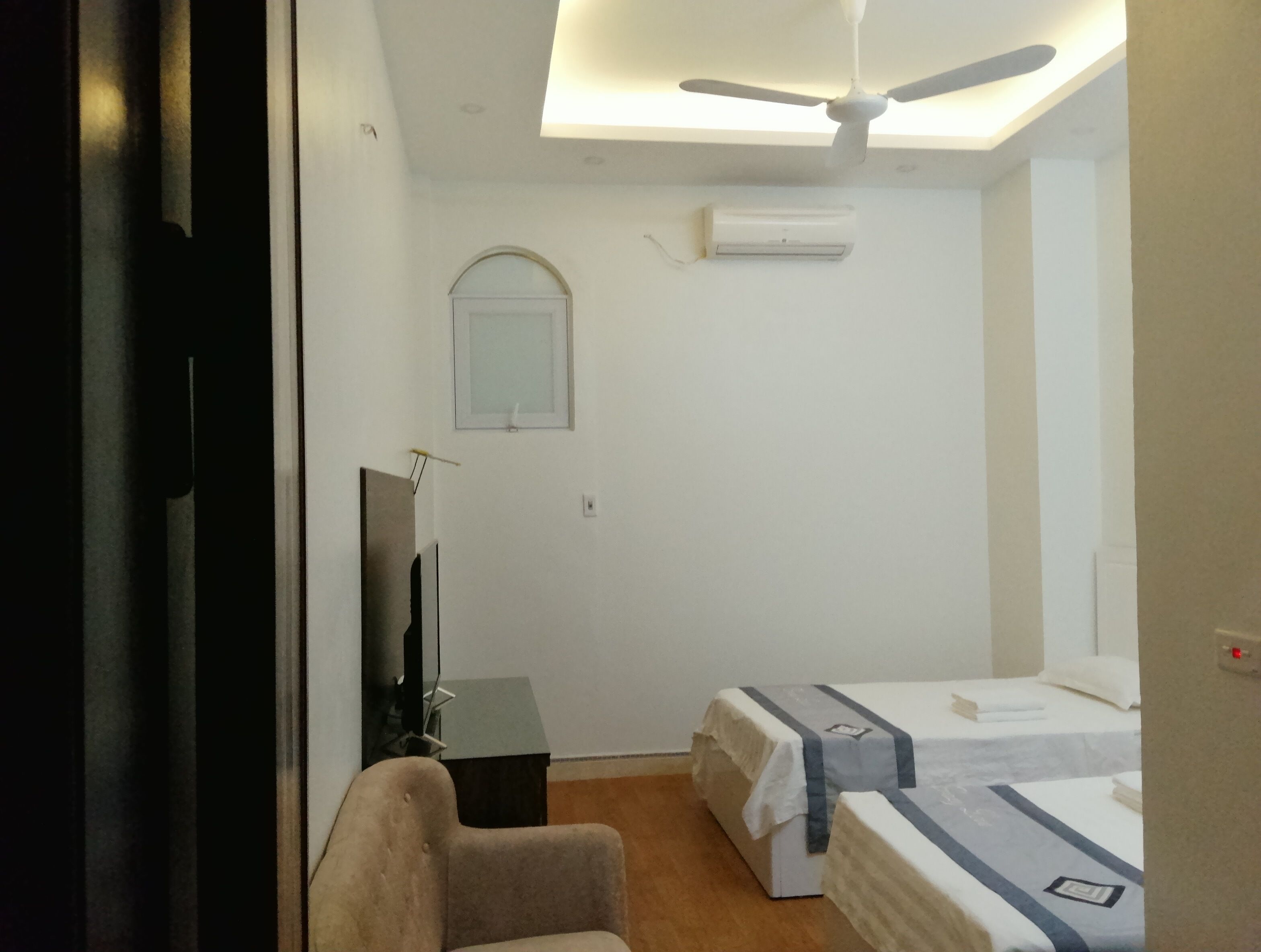 A hotel room with a ceiling fan, a flat-screen TV, a small desk, and two beds with white bedding.