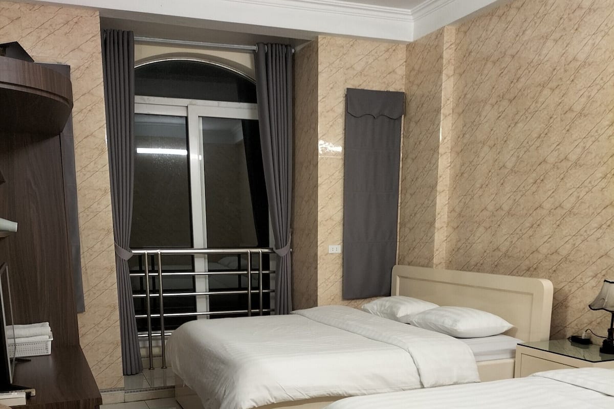 A hotel room with two beds, a desk, a chair, and a window with curtains.