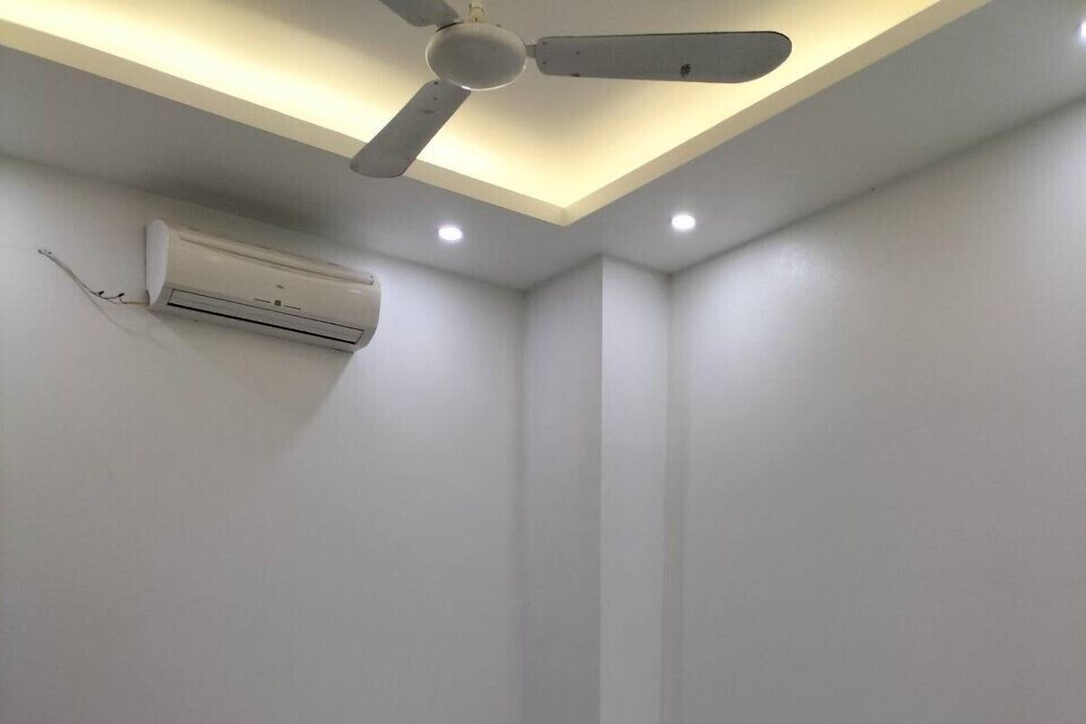 A small, white, two-bed room with a ceiling fan, an air conditioning unit, and a bedside table with a lamp.