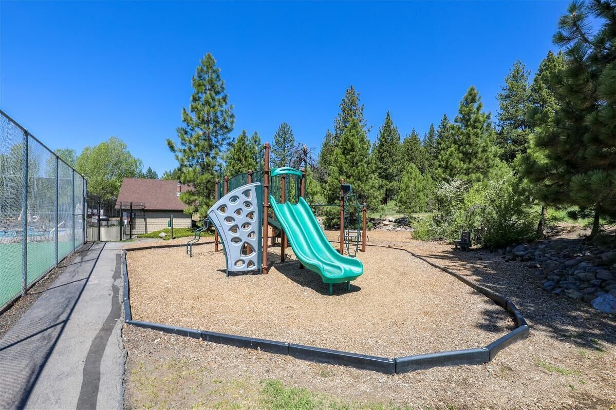 Un terrain de jeux avec un toboggan et une structure d’escalade, le tout entouré d’arbres.