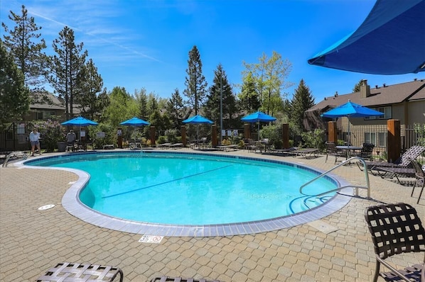 A swimming pool with lounge chairs and umbrellas, surrounded by trees and buildings.