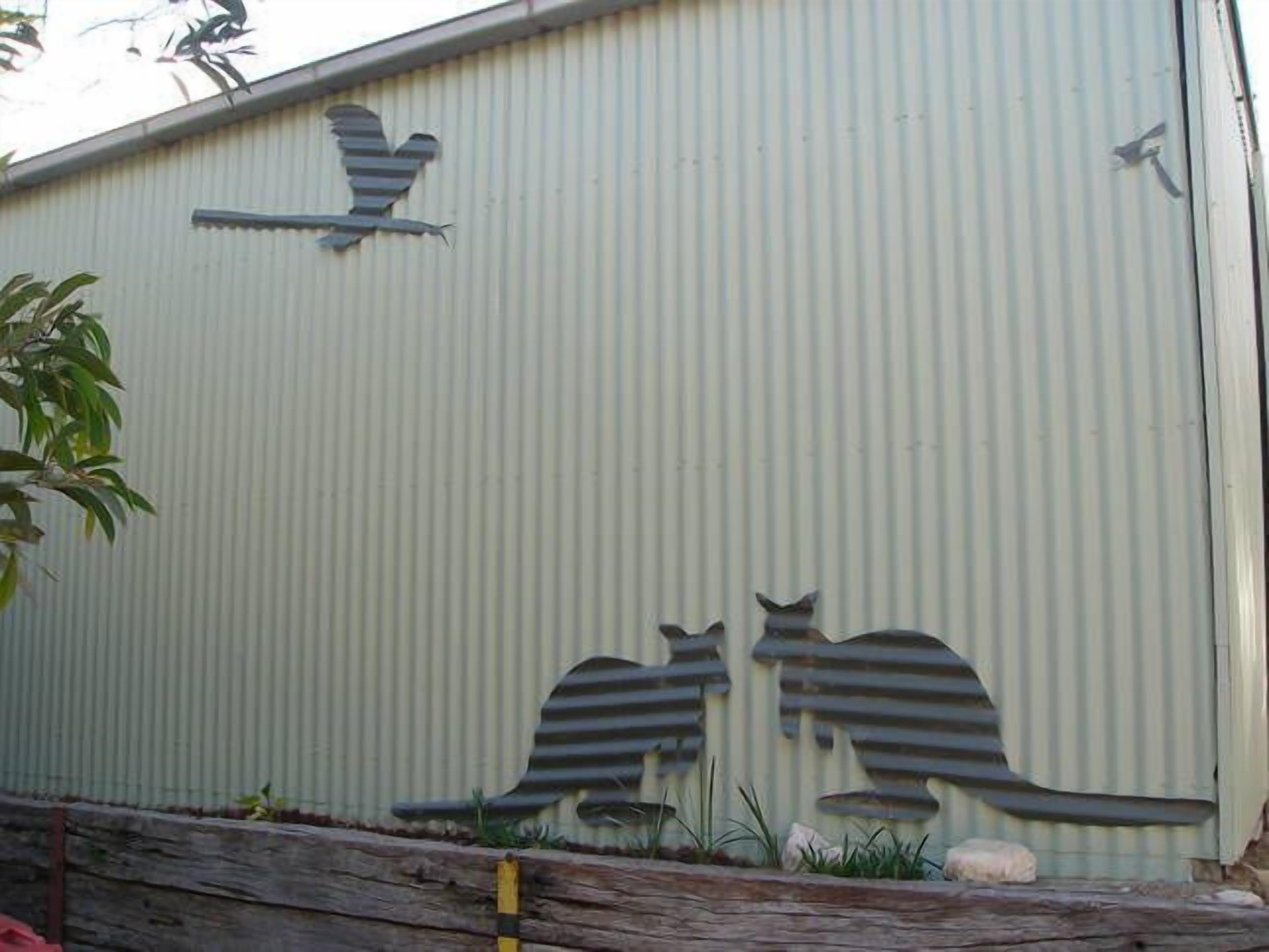 A corrugated metal wall with bird and cat cutouts.