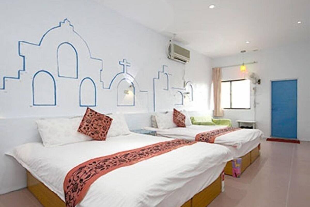 A hotel room with two beds, a blue door, and a window with curtains.