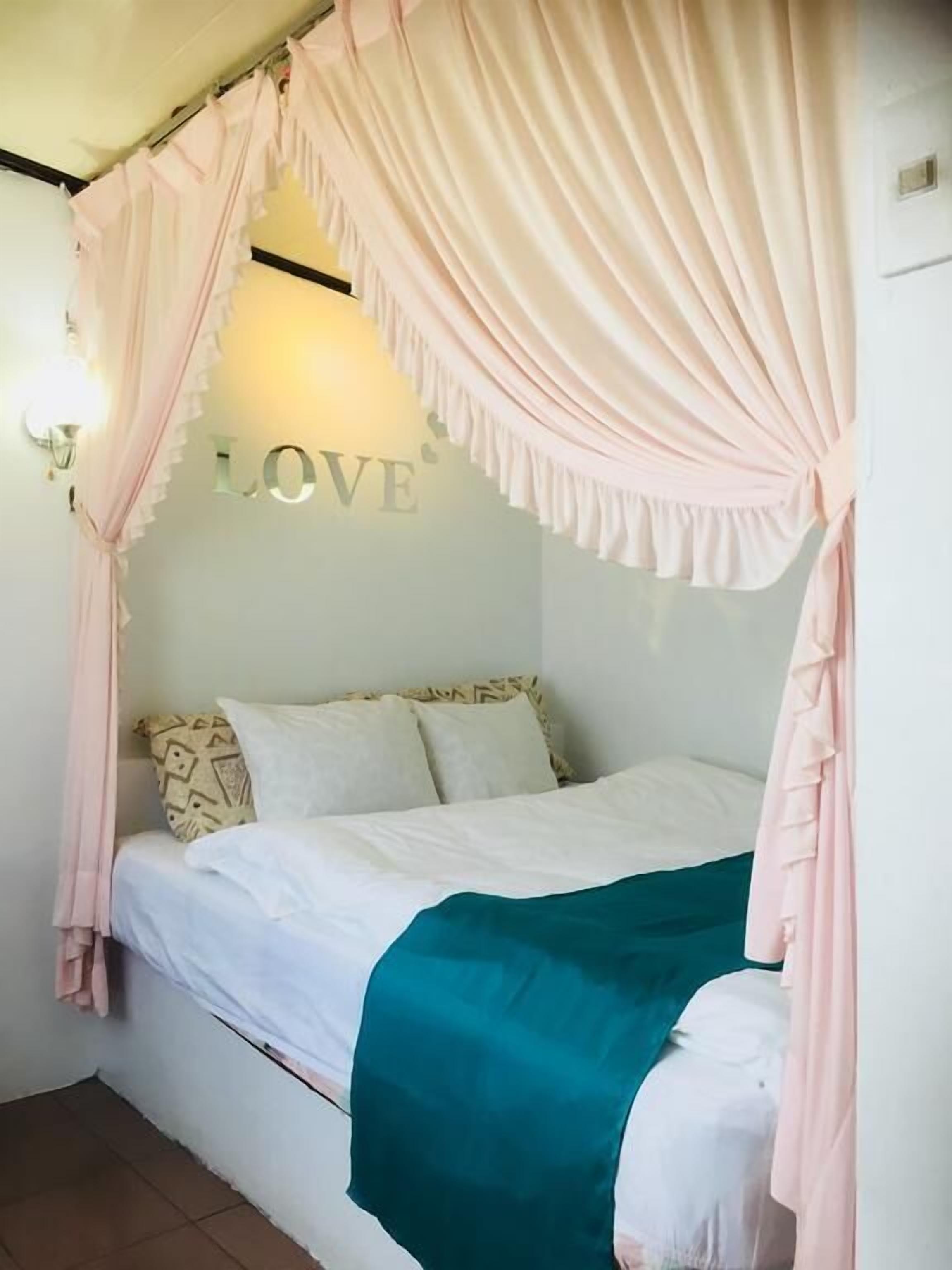 Une chambre avec un lit à baldaquin, une lampe fixée au mur et un panneau décoratif portant le mot « AMOUR ».